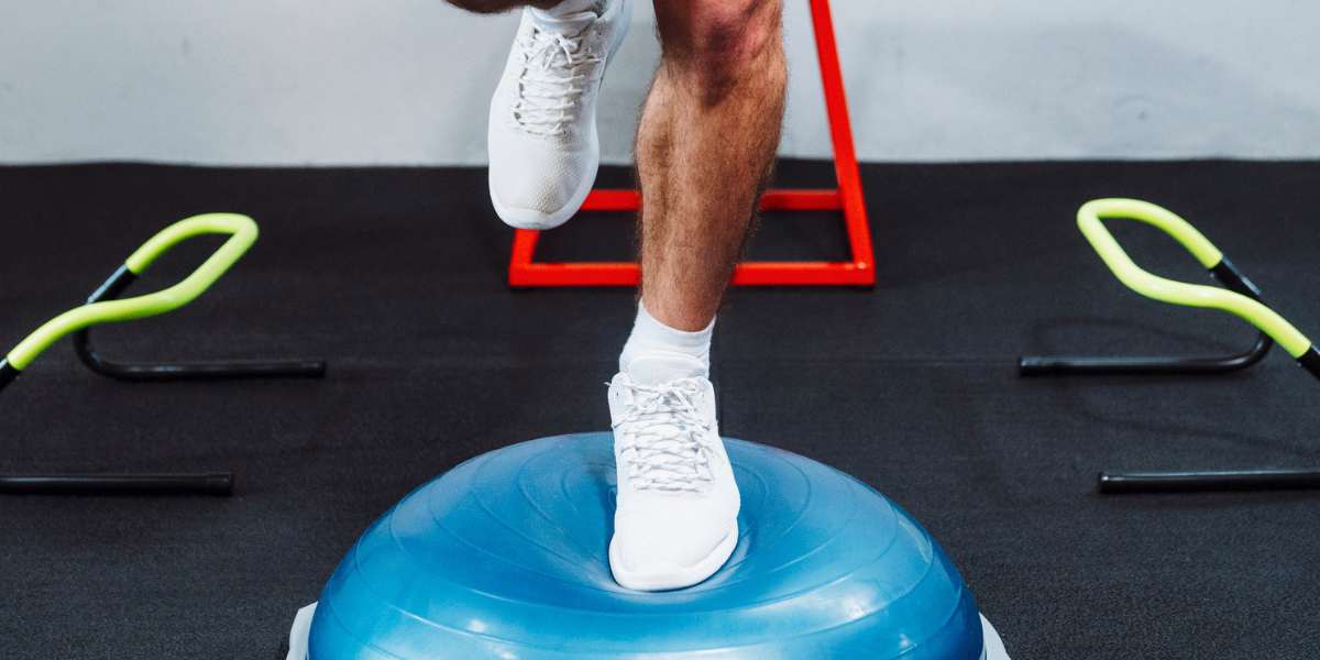 Male balancing on a half balance ball in a gym setting.