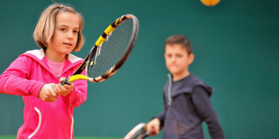 Image of young tennis players getting a lesson from a tennis pro on an indoor court.