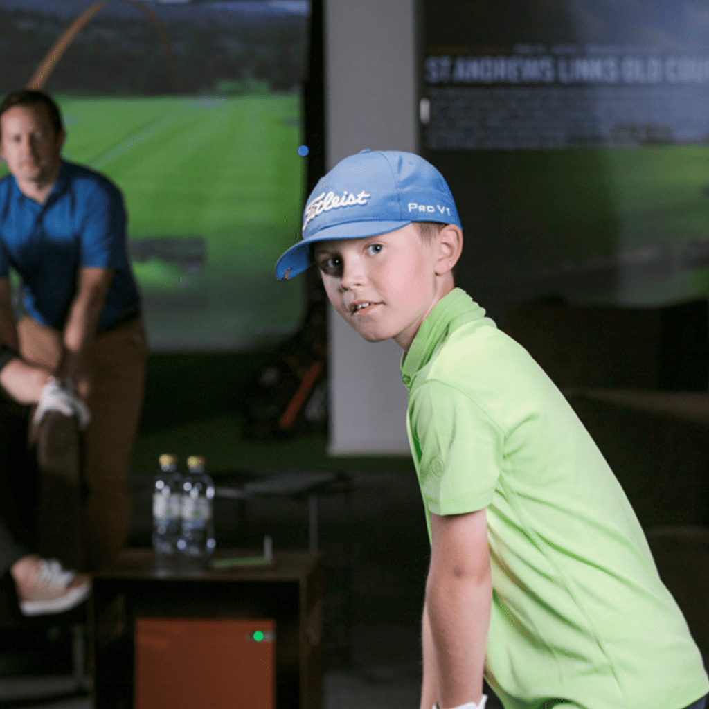 Kid playing golf on an indoor golf simulator with parents watching.