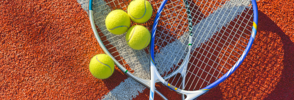 Close of tennis racquet with balls on clay court.